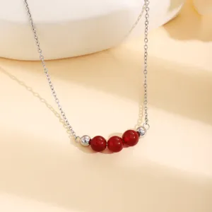 Gros plan d'un collier en chaîne argentée avec des perles rouges sur fond crème élégant.