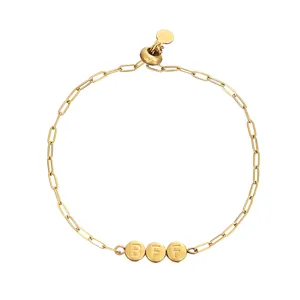 Dettaglio di bracciale con catena paperclip dorata e ciondoli con lettere BFF incise.