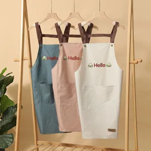 Detailansicht von Küchenschürzen aus Stoff mit Hello-Druck, Kreuzträgern und Vordertaschen.
