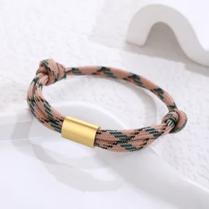 Detailed shot of a braided rope bracelet with a gold metal tube clasp on white tray.