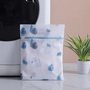 Durable white mesh laundry bag with blue leaf print and zipper closure for washing.