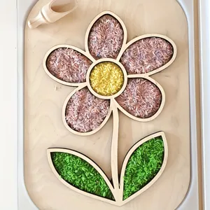 Hölzernes blumenförmiges Tablett mit buntem Reis und Löffel für sensorisches Spiel und Deko.