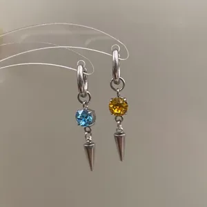 Close-up detail of handmade metal hoop earrings with colorful crystal gems and cone pendants.