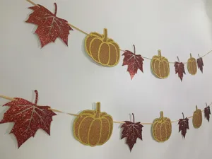 Detalle en primer plano de guirlande colgante con hoja de arce y calabaza con purpurina.