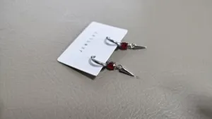 Detailed shot of silver hoop earrings with red crystal and cone pendant on a white jewelry card.