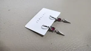 Close-up detail of silver hoop earrings with red crystal and spike pendant on jewelry card.