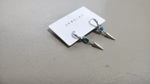 Detail shot of silver spike drop hoop earrings with blue crystal rhinestones on white card.