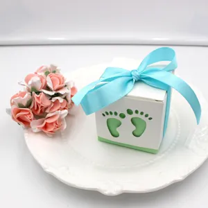 Closeup of cute white baby favor candy box with blue ribbon and footprint cutout on plate.