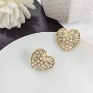 Primo piano dei dettagli di orecchini a cuore dorati con perle e strass su piatto.