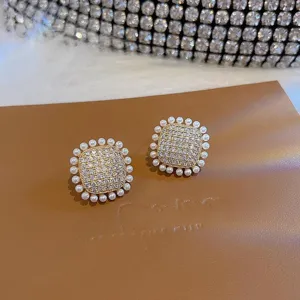 Primo piano dettagliato di eleganti orecchini quadrati in strass bordati con perle delicate.