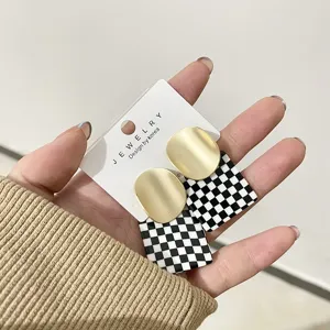 Close-up detail of stylish matte gold and black white checkerboard acrylic earrings display.