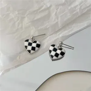 Detailed shot of black and white checkerboard heart stud earrings with silver needle.
