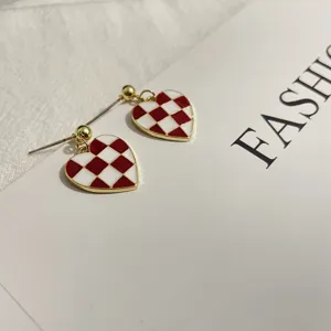 Close-up detail of stylish red and white checkerboard heart earrings with silver needle.