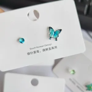 Nahaufnahme der asymmetrischen blauen Schmetterling- und Kristall-Ohrstecker auf der weißen Karte.