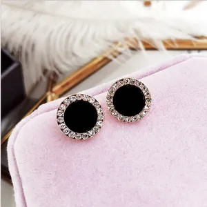 Close-up van elegante ronde oorbellen met strass en zwart centrum op roze sieradendoos.