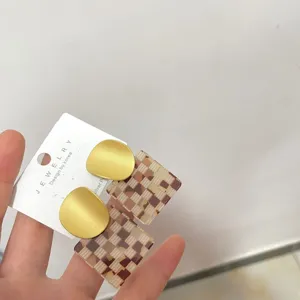Detailed close-up of matte gold and checkered acrylic earrings on display card.