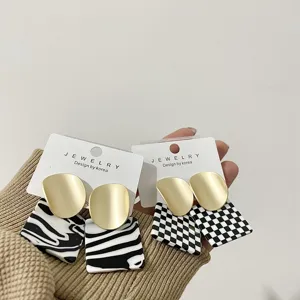 Detailed shot of geometric acrylic and matte gold drop earrings with zebra and check patterns.