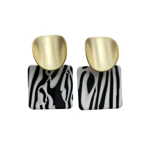 Close-up of stylish geometric drop earrings with matte gold top and black white acrylic square base.
