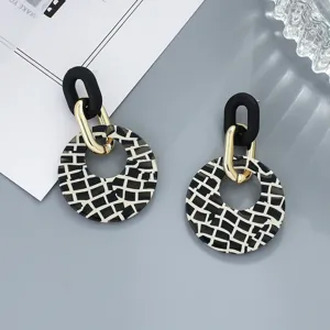 Close-up details of geometric acrylic black and white grid earrings with chic metal links.