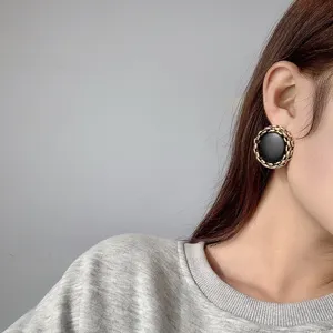 Close-up detail of vintage black leather and metal chain round stud earrings for women.