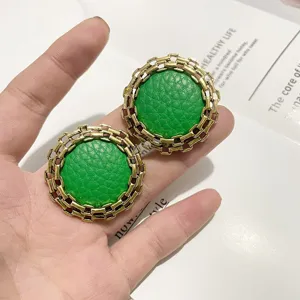 Detailed view of vintage gold metal chain rimmed green leather round earrings stylish design.