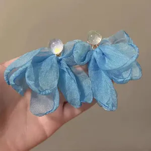 Close-up detail of blue sheer fabric flower earrings, elegant fairy style seaside jewelry.
