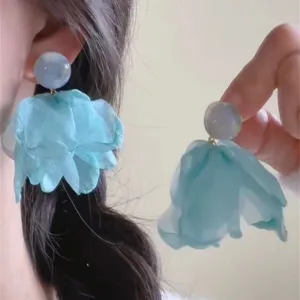 Detailed close-up of light blue fabric flower petal earrings, elegant seaside resort style.