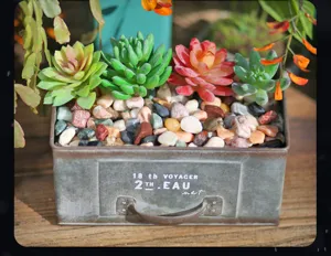 Artificial succulent plants potted in retro metal container with colorful decorative pebbles.