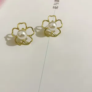 Minimalist gold flower pearl earrings detail shot, elegant hollow design with glowing pearl.