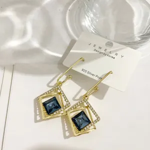 Detailaufnahme geometrischer Goldohringe mit blauem Kristall und Strass auf Karte elegant.