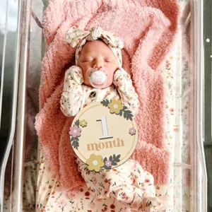 Wooden baby milestone card detail showing 1 month design with floral pattern for newborn photo.