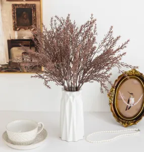 Détail de branche de pin brumeux artificiel dans un vase blanc pour deco interieure chic.