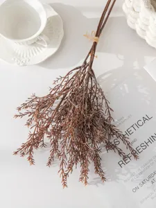 Gros plan détaillé d'un bouquet de branches de pin artificielles brunes sur table blanche.