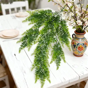 Artificial fern vine hanging plant detail showing lush green leaves on white wooden table.