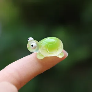 Miniature green resin sea turtle figurine on finger showing tiny scale for micro landscape decor.