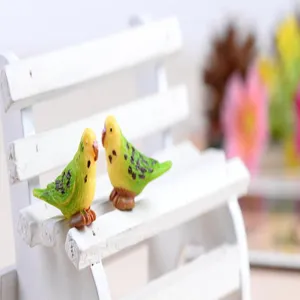 Close-up detail of cute mini resin parrot figurines on white bench for miniature garden decor.