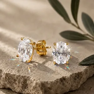 Makroansicht von ovalen Ohrsteckern mit Zuchtdiamanten in Goldfassung auf Steinoberfläche.