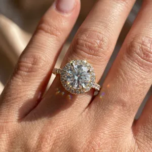 Close-up of a sparkling moissanite halo engagement ring on a finger with warm sunlight