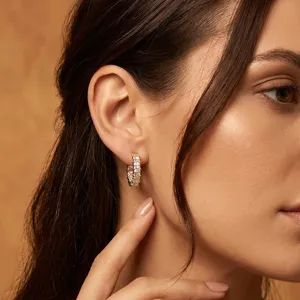 Detalle de pendientes de aro dorados de lujo con cristales cuadrados brillantes