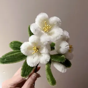 Closeup detail of handmade white pipe cleaner flowers with yellow stamens and green leaves.
