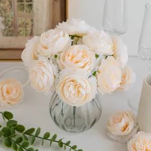 Closeup view of artificial champagne peonies in clear glass vase with delicate props.