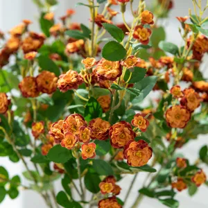 Close-up detail of artificial small rose flower branches with green leaves for home decor.