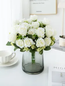 Detail view of artificial white rose bouquet with green leaves in grey glass vase, home decor.