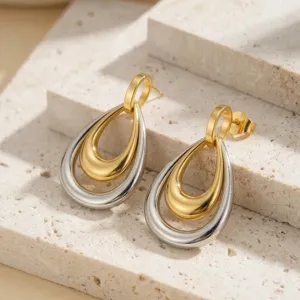 Elegantes pendientes de gota bicolores en acero inoxidable sobre un soporte de piedra