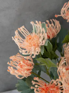 Close-up detail of artificial flocked orange spider chrysanthemum flower with green leaves.