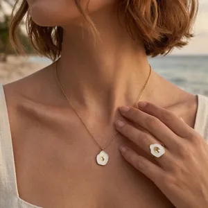 Primo piano di un elegante set di collana e anello con ciondolo a conchiglia in smalto bianco.