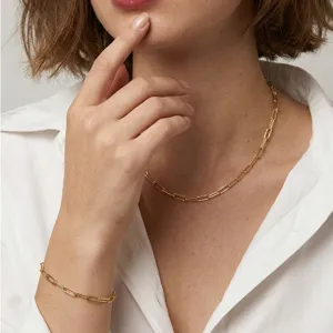Detail view of a gold paperclip chain necklace and bracelet set on a female model.