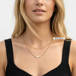 Gros plan d'un collier croix minimaliste plaqué or 14 carats porté par un mannequin chic
