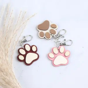 Detail view of wooden paw print keychains, featuring three color variants with metal clasps.