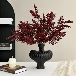 Flores artificiales de guirnalda roja con jarrón de cerámica negra para decoración.